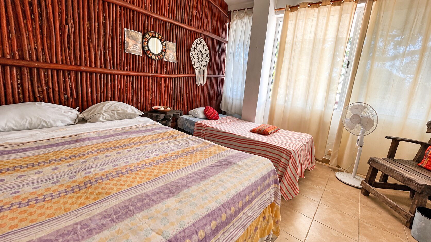 Habitación de hotel con dos camas, pared de madera, espejo, mesita de noche y un ventilador.