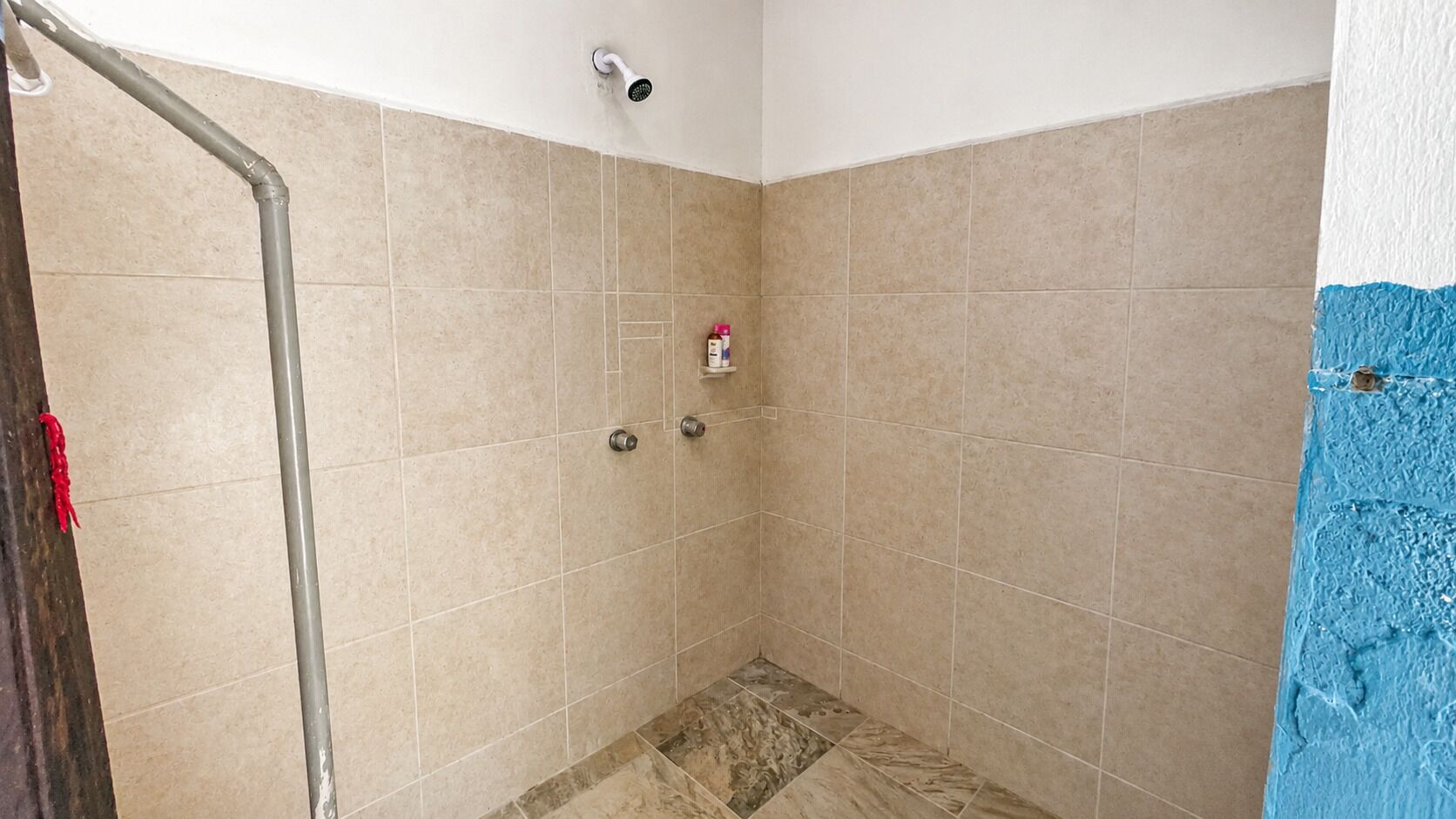 Zona de ducha con azulejos color beige, un cabezal de ducha y un pequeño estante con artículos de aseo.
