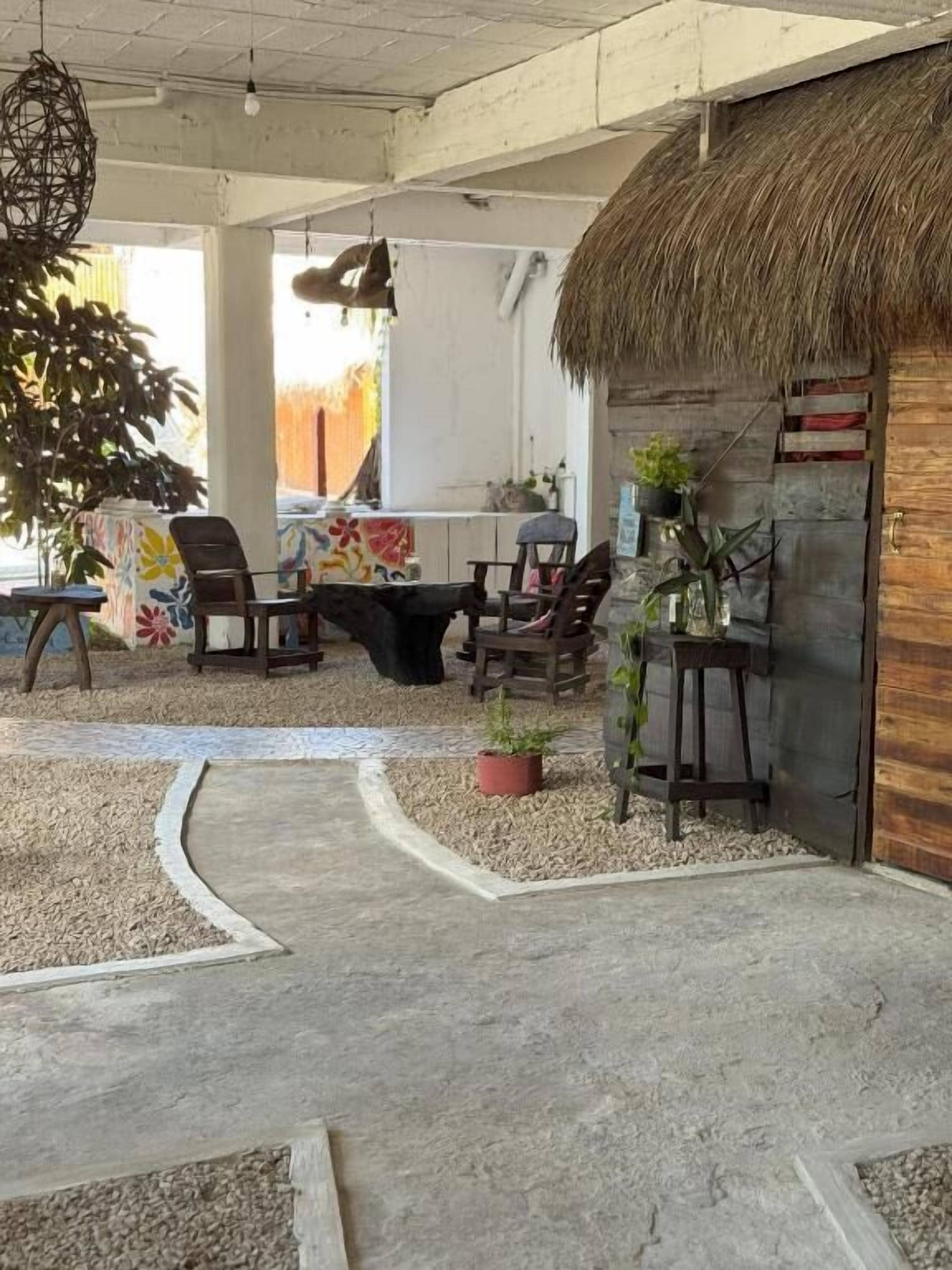 Un espacio al aire libre con mesas y sillas, una estructura con techo de paja y plantas en macetas.