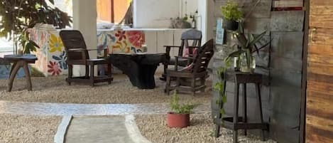 Un espacio al aire libre con mesas y sillas, una estructura con techo de paja y plantas en macetas.