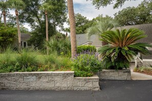 A residential area with a stone retaining wall, various plants, and trees. - Double Bogey by Sandpiper | Near Beach (Seabrook Island)