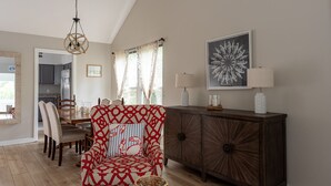 Uma sala de estar com uma poltrona estampada, um aparador de madeira e um espaço de jantar com cadeiras e uma mesa.