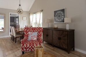 A living room with a patterned armchair, a wooden cabinet, and a dining area with chairs and a table. - Double Bogey by Sandpiper | Near Beach (Seabrook Island)