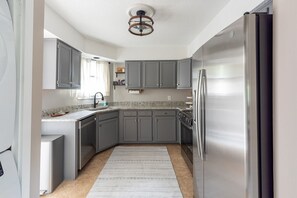 A compact kitchen with grey cabinets, a stainless steel refrigerator, and a granite countertop. - Double Bogey by Sandpiper | Near Beach (Seabrook Island)