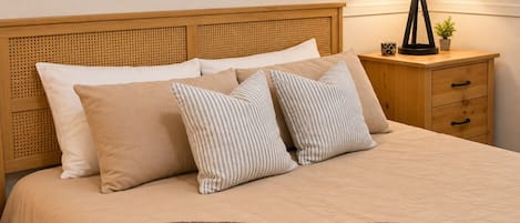 A neatly made bed with a brown blanket, a headboard with a woven pattern, and a bedside table with a lamp and a small plant.