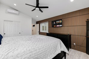 Ein Schlafzimmer mit einem Bett, Deckenventilator, einem an der Wand montierten Fernseher und einer Holzwand.