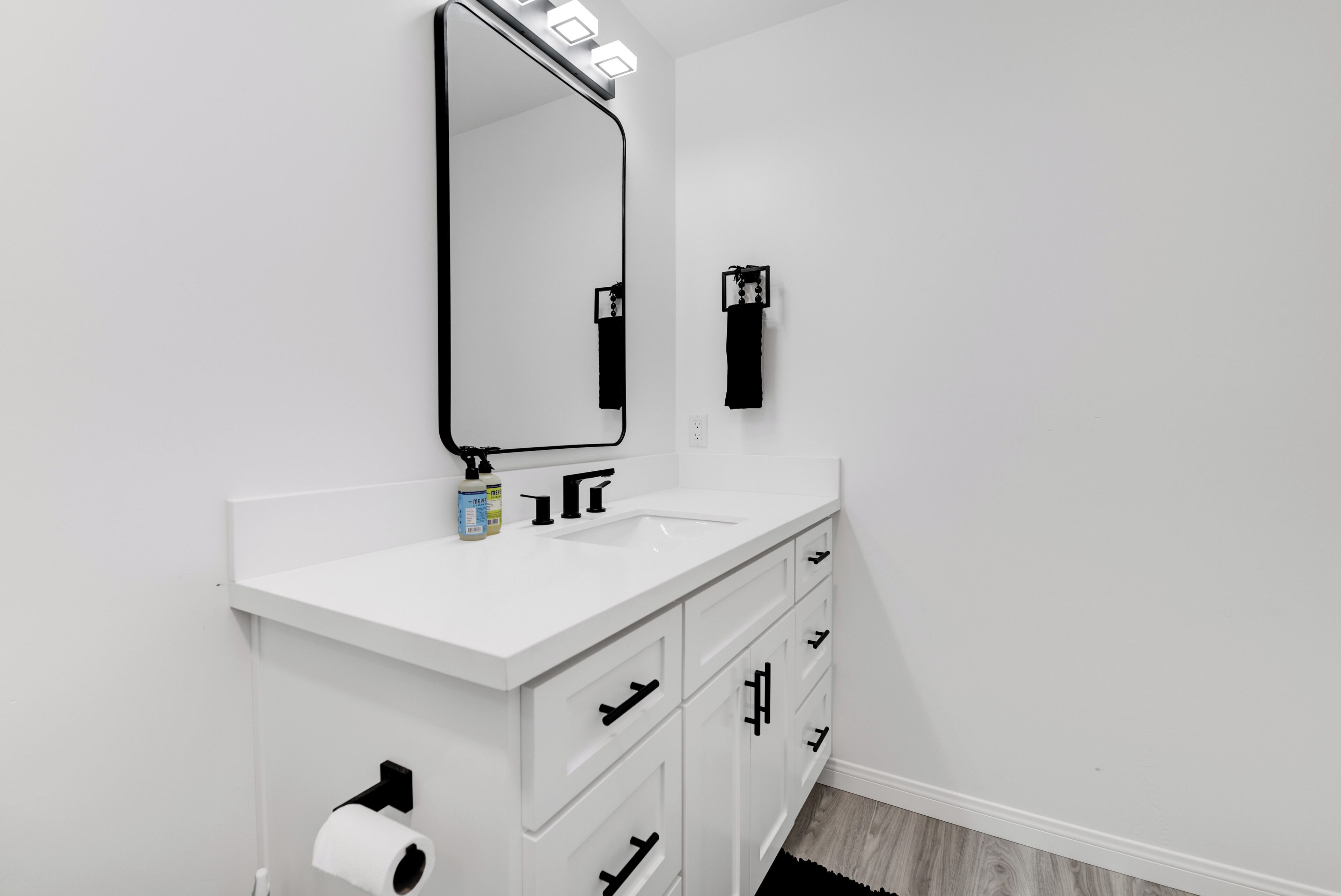 Un baño moderno con tocador blanco, un espejo con iluminación, toallero y dispensador de papel higiénico.