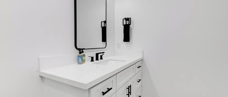 Un baño moderno con tocador blanco, un espejo con iluminación, toallero y dispensador de papel higiénico.