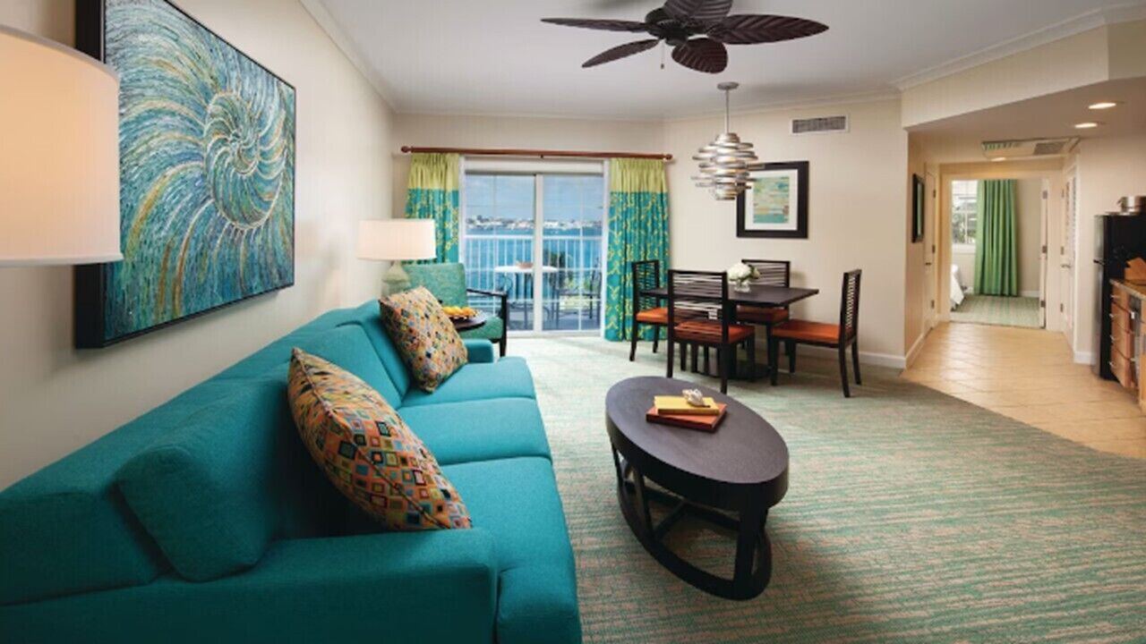 A living room with a teal sofa, a dining table, and a ceiling fan.