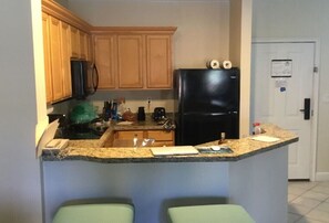 Eine Küche mit Holzausstattung, einem schwarzen Kühlschrank, einer Granit-Arbeitsplatte und einer kleinen Kücheninsel mit zwei grünen Barhocker.