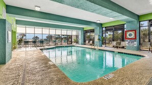 En indendørs swimmingpool med glasvægge, flisegulv og et skilt til livredder.