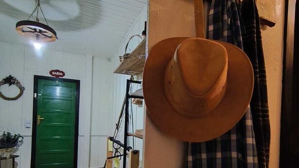 Una habitación con una puerta verde, un sombrero colgado y un mantel a cuadros.