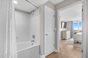 Ein modernes Badezimmer mit Badewanne, Dusche und einem begehbaren Kleiderschrank, der in einen Schlafbereich mit Bett und Kommode führt.
