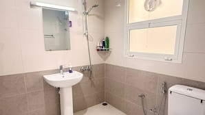 Et badeværelse med en hvid vask, toilet, bruser og et spejl.