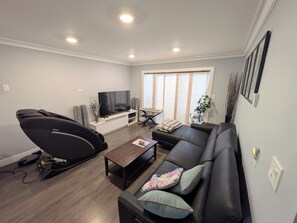 A living room with a black sofa, a coffee table, a TV on a stand, a keyboard, and a plant. - The Bloom House - 2 Bedroom 2 Bath Family Home (Vancouver)