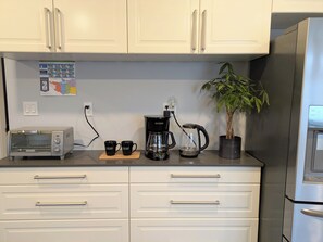 A kitchen with white cabinets, a toaster, a coffee maker, and a potted plant. - The Bloom House - 2 Bedroom 2 Bath Family Home (Vancouver)