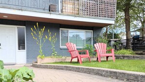 Een woonhuis met een veranda, twee rode Adirondack-stoelen en een kleine tuin met gele bloemen.