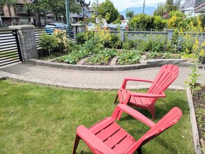 A garden with a paved walkway, a stone wall, and a red chair. - The Bloom House - 2 Bedroom 2 Bath Family Home (Vancouver)