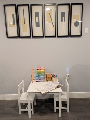 A room with a white table, two white chairs, a wooden toy abacus, a cup with pencils, and a framed abstract artwork on the wall. - The Bloom House - 2 Bedroom 2 Bath Family Home (Vancouver)