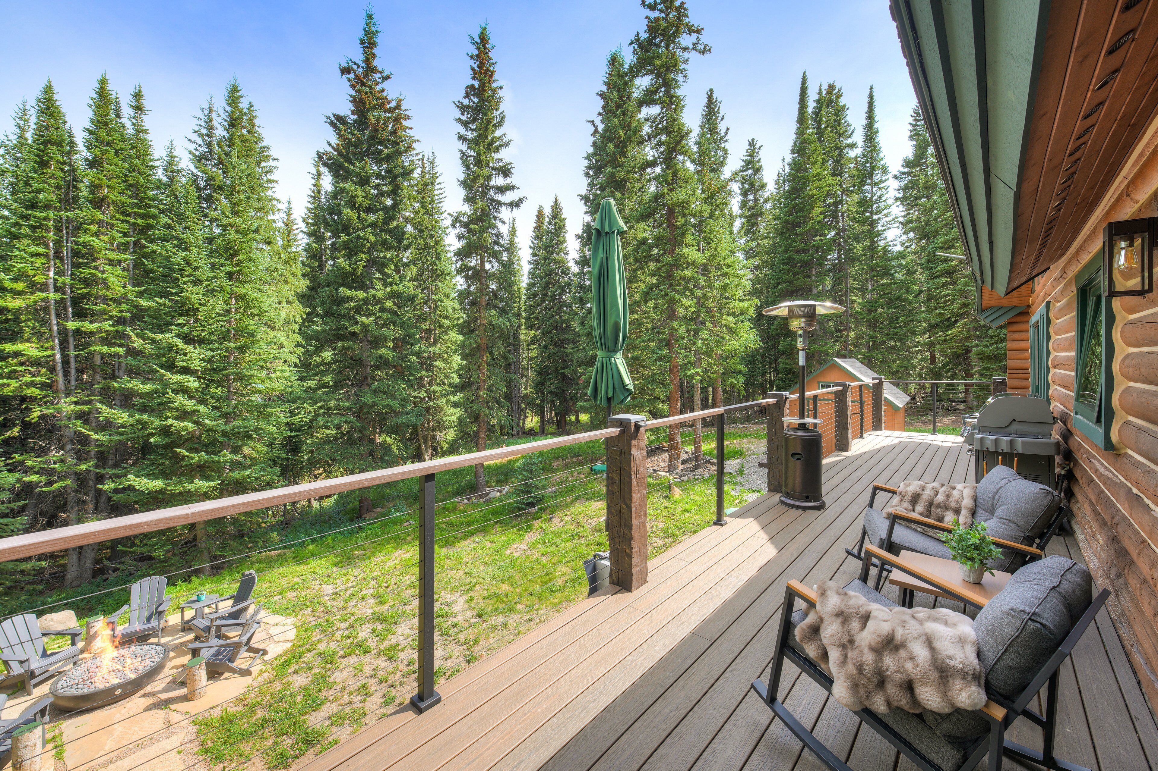 Une terrasse en bois avec des meubles d’extérieur, un foyer et une vue sur une forêt.