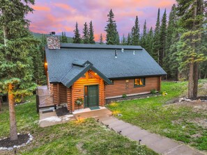 A log cabin with a stone chimney, a green door, and a small porch. - Mountain Chic Cabin | Hot Tub, Firepit & Seclusion in Blue River (Blue River)