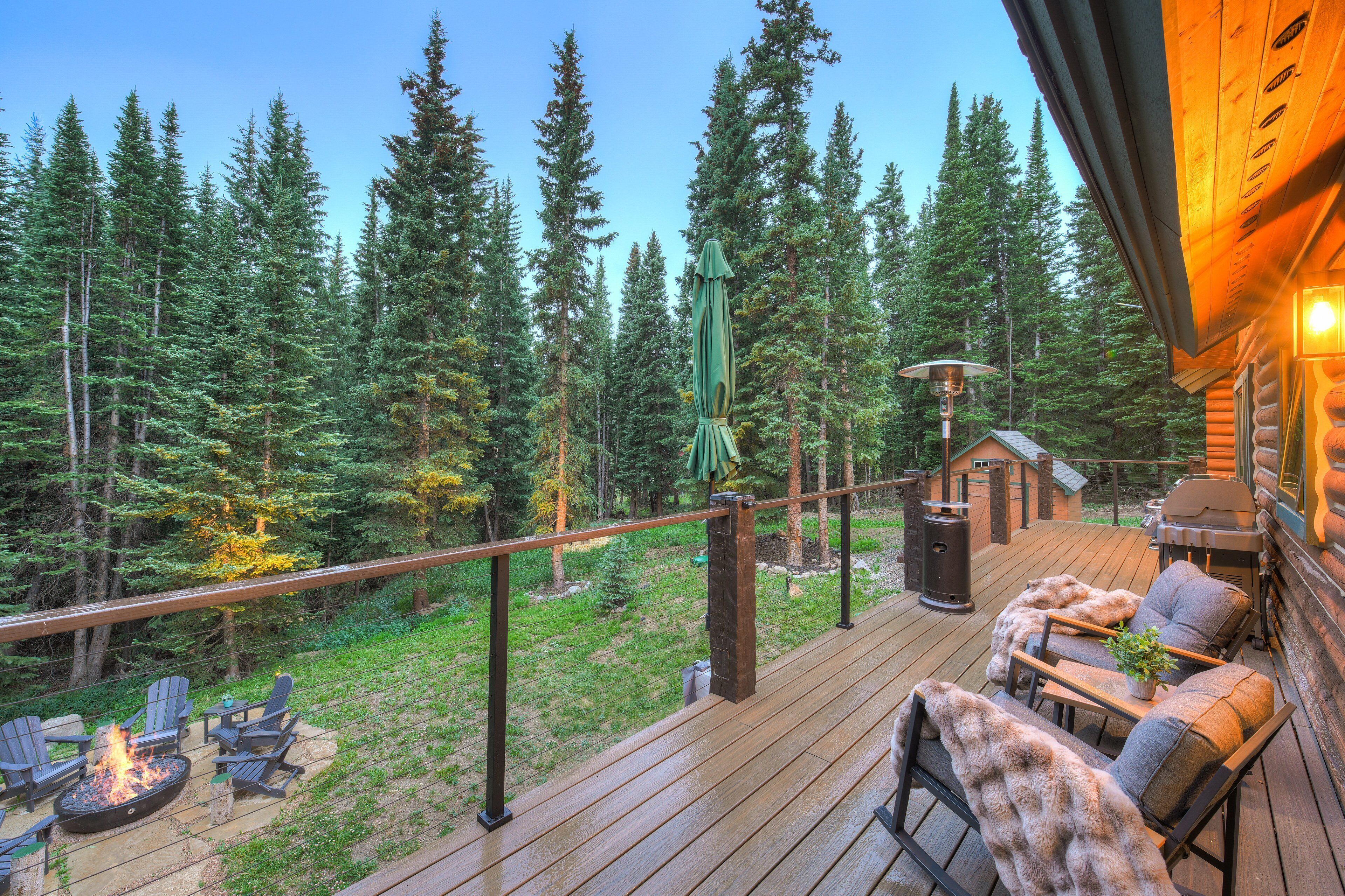 A wooden deck with outdoor furniture, a fire pit, and a view of a forest.