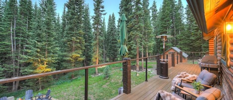 A wooden deck with outdoor furniture, a fire pit, and a view of a forest.
