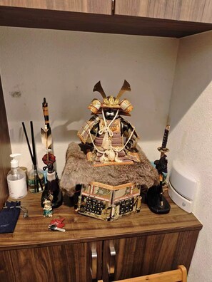 Ein Holztisch mit einer Samurai-Statue, einem mit Fell bezogenen Hocker und verschiedenen persönlichen Gegenständen.