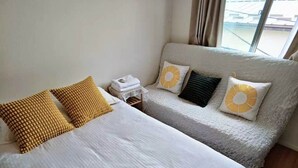 A hotel room with two beds, a nightstand, and a window with a view of buildings. - Sakura Villa (Sumida City)