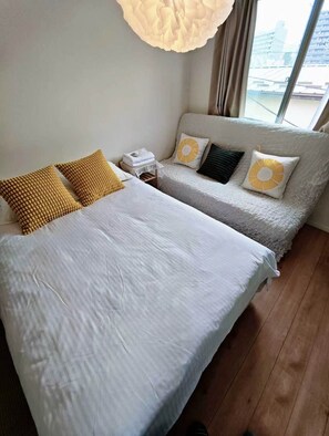 Ein Hotelzimmer mit zwei Betten, einem Nachttisch und einem Fenster mit Blick auf Gebäude.