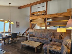 A spacious living area with a wooden staircase, a patterned sofa, a dining table with chairs, and a coffee table. - 2BR/2B Condo with Hot Tub/Pool access. 4.5 Miles to Jackson Hole Mountain Resort (Wilson)