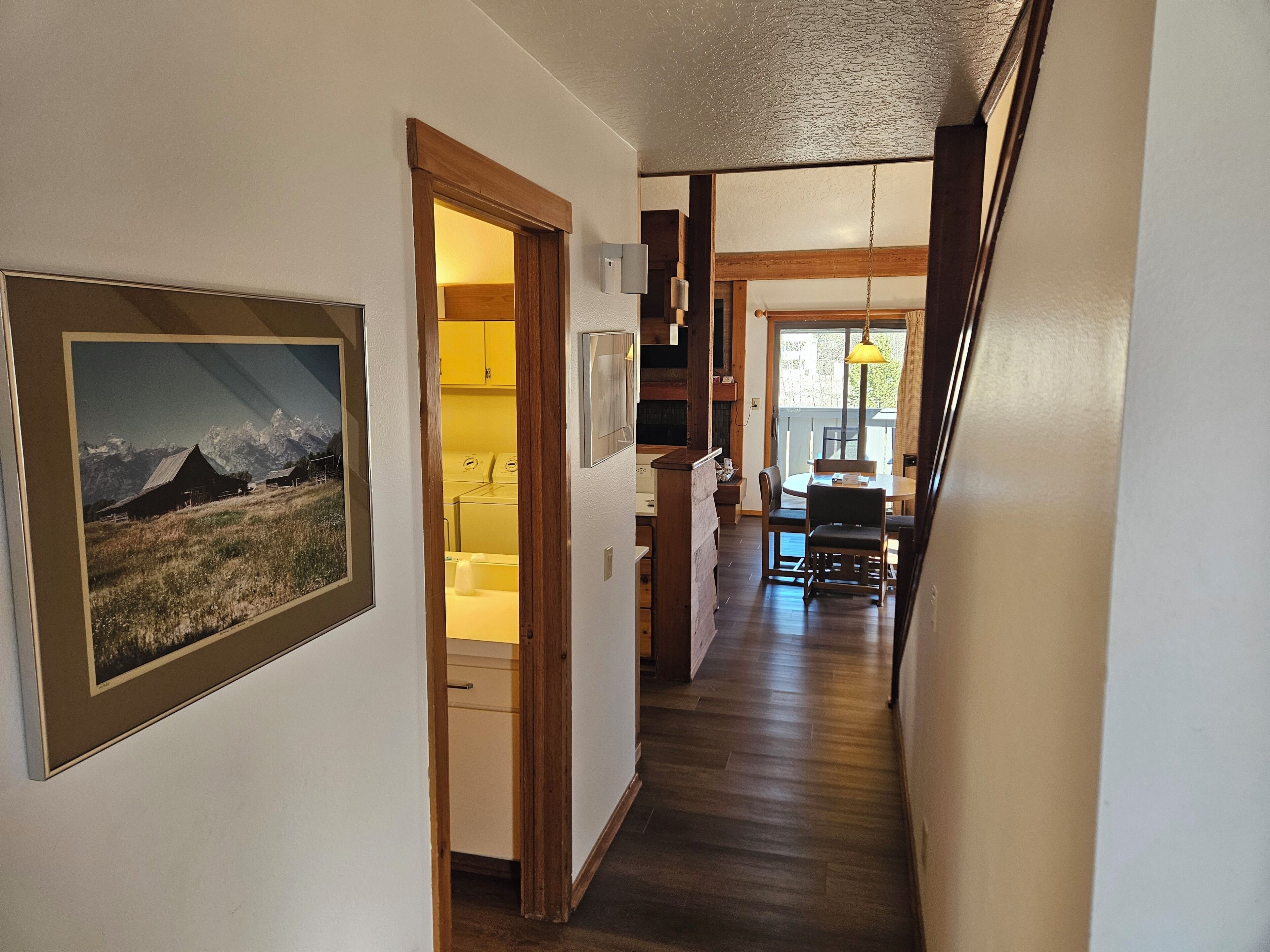 A hallway with a framed picture, a laundry area, and a dining area with a table and chairs.