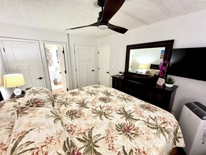 A bedroom with a bed, a ceiling fan, a dresser, a mirror, and a wall-mounted TV. - South Kihei Luxury Condo • Gorgeous Sunset Views. Steps to Kamaole Beach III (Kihei)
