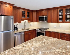 A modern kitchen with granite countertops, stainless steel appliances, wooden cabinets, and a microwave. - South Kihei Luxury Condo • Gorgeous Sunset Views.  Steps to Kamaole Beach III (Kihei)