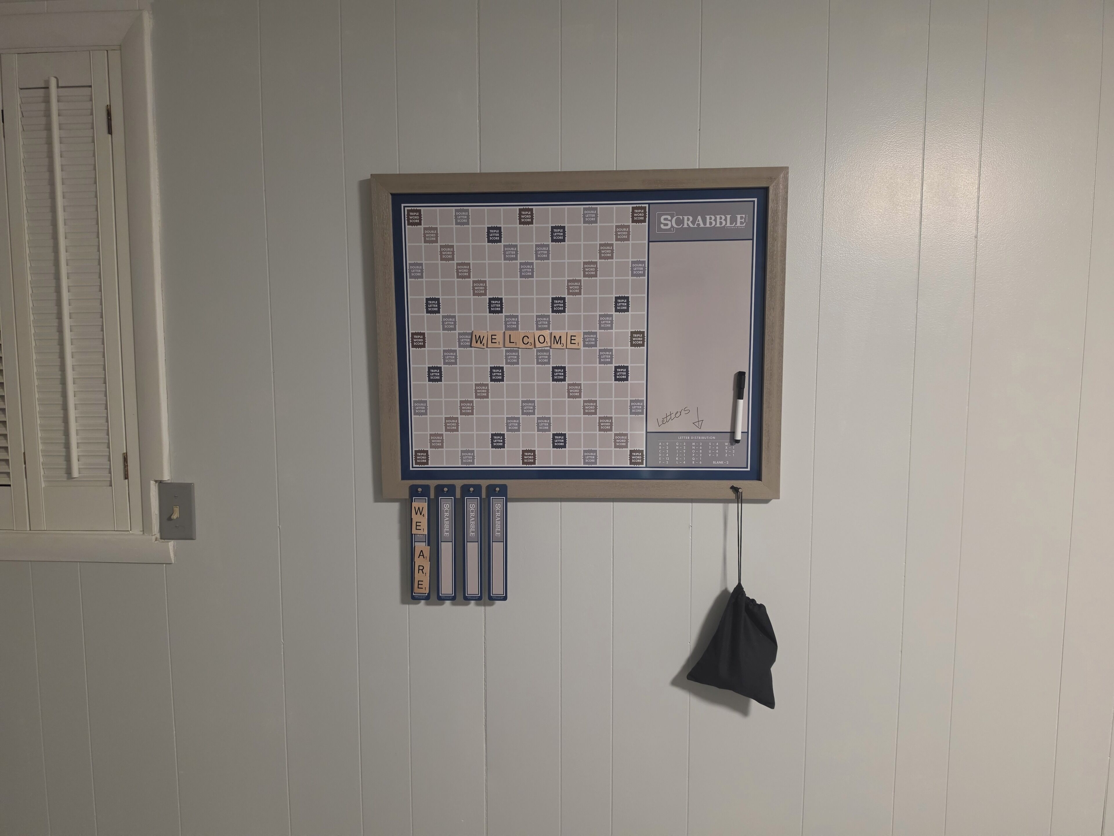 Un gioco da tavolo Scrabble allestito su una parete, con tessere e lettere appese sotto.