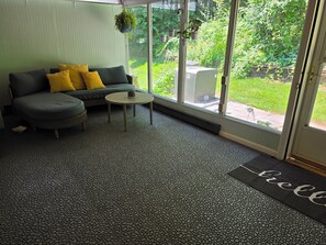 A room with a grey sofa, a small round table, and a large window with a view of greenery. - 5 min to Penn State, Airport. King Bed, Game Room, Breakfast. Family Friendly! (State College)