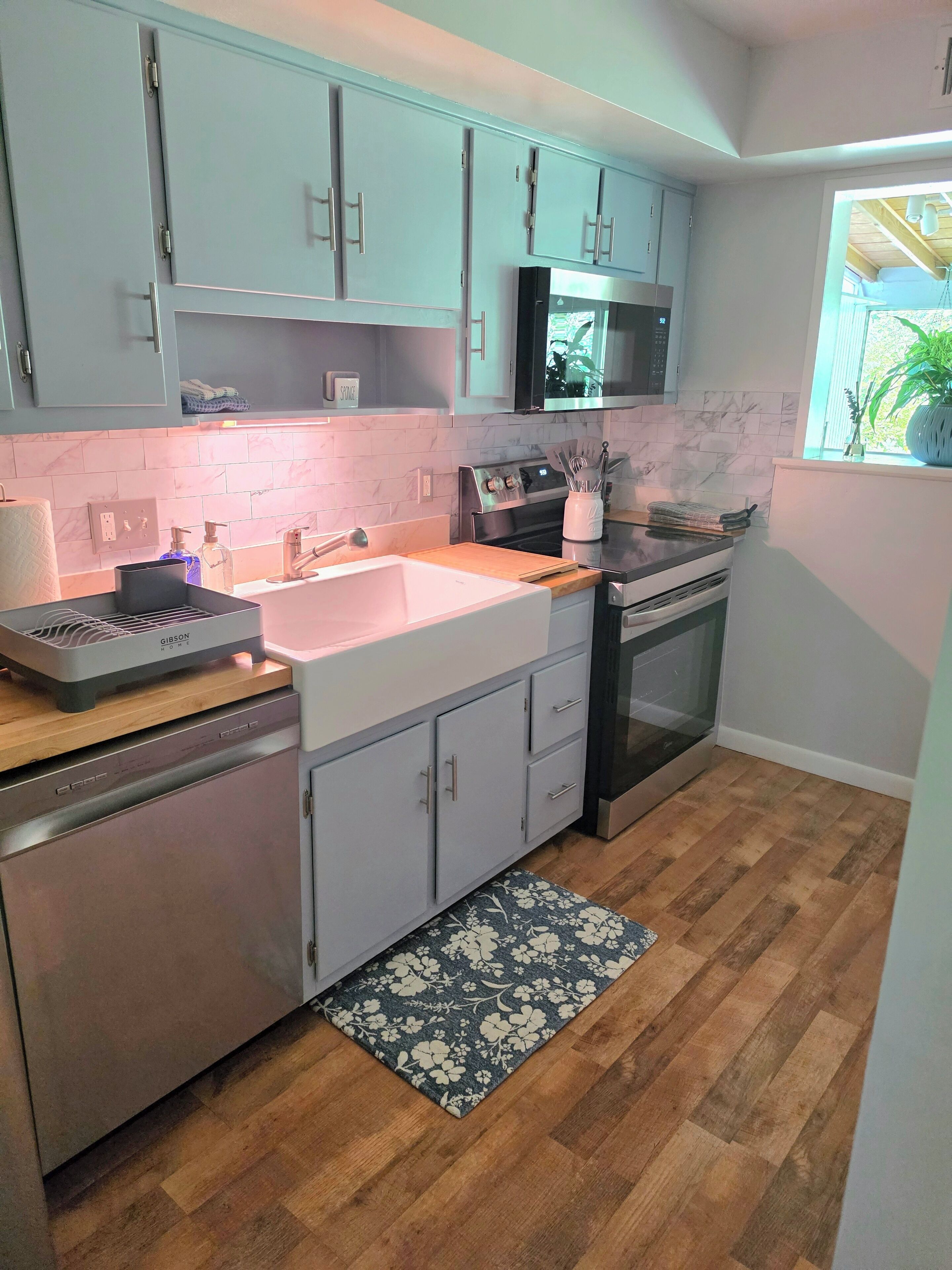 A modern kitchen with light blue cabinets, a stainless steel dishwasher, a microwave, and an oven.