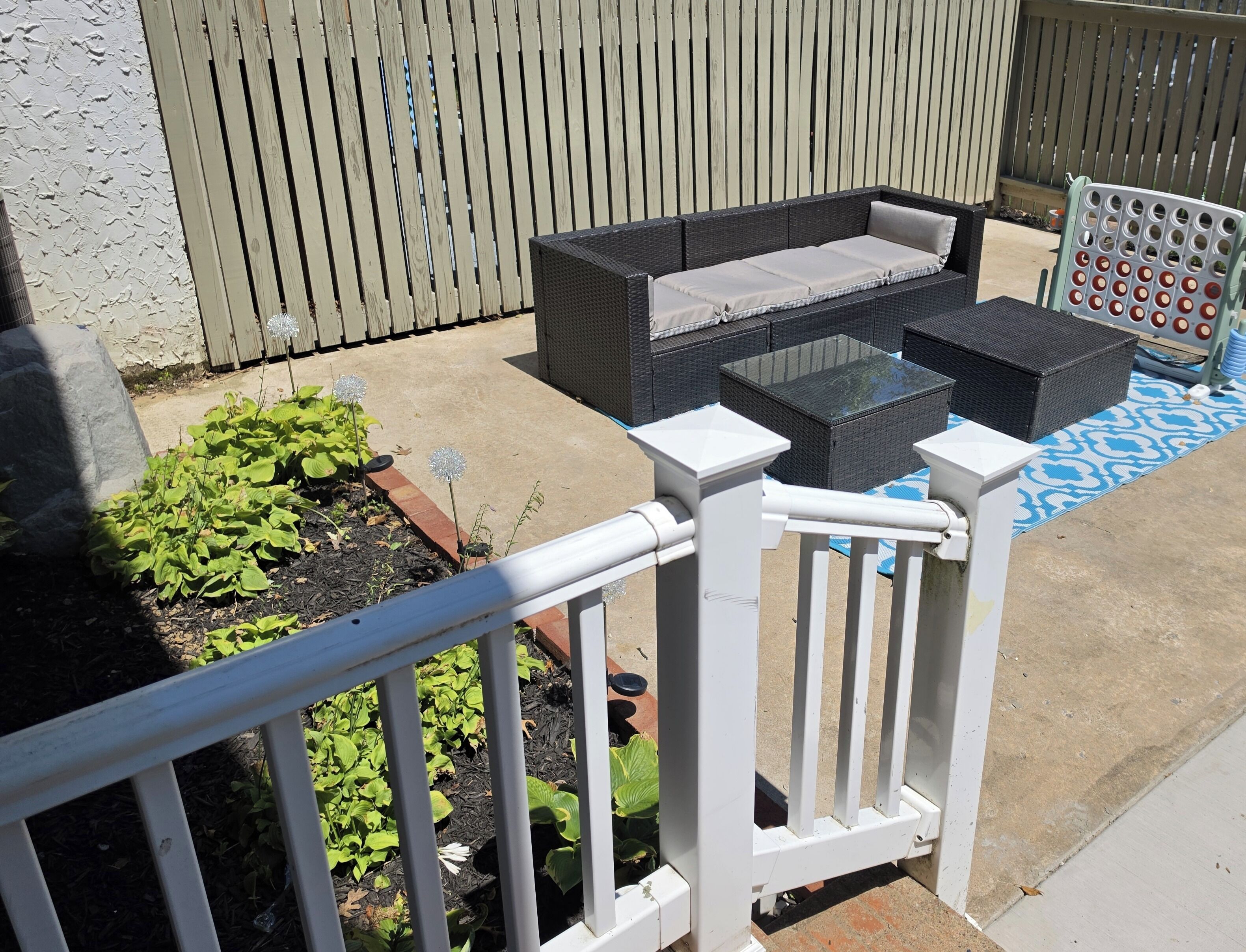 An outdoor patio with a wicker sofa, a glass-top table, and a white railing.