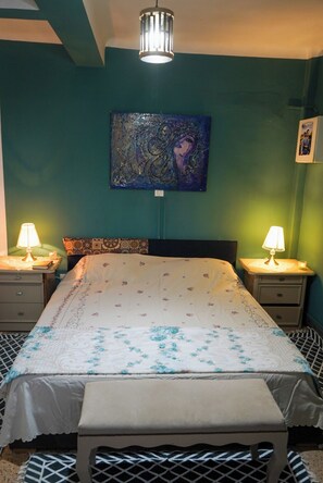 A bedroom with a bed, two bedside lamps, a nightstand, a bench, a painting on the wall, and a ceiling light fixture. - Comfortable Apartment in the Heart of Tunis – Explore the City Easily (Tunis)