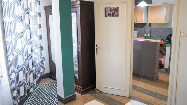 Ein Flur mit gemusterten Vorhängen, einer Holztür und einer Küchenzeile mit Schränken und einem Kühlschrank.