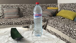Ein Wohnzimmer mit einem gemusterten Sofa, einem Tisch mit einer Wasserflasche, einem Teller Essen und Wanddekorationen.