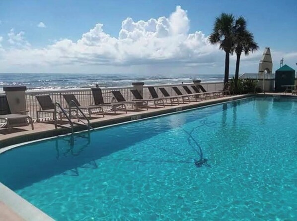 Una piscina azul cristalina con sillas de descanso y vista al océano.