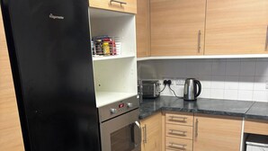 A kitchen with a black refrigerator, a toaster, a kettle, and wooden cabinets. - One Bedroom Home In Greenwich Peninsular (London)