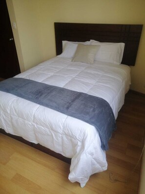 Ein Bett mit dunklem Kopfteil, weißer Bettwäsche und einer blauen Decke.