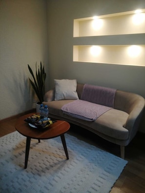Ein Wohnzimmer mit einer Couch, einem Couchtisch mit Snacks, einer Topfpflanze und einer Wandleuchte.