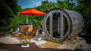 Une structure cylindrique en bois dotée d’une porte en verre, d’un jacuzzi et d’une terrasse en bois avec des chaises longues.