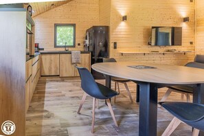 A wooden interior with a dining table, chairs, a kitchen area, and a window. - Le Chalet Marmotte - LA BOURBOULE (LA BOURBOULE)