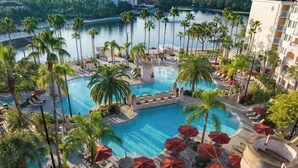 Een resort met een centraal gelegen zwembad, omringd door palmbomen en ligbedden.