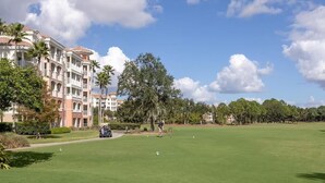 Een golfbaan met een clubhuis, palmbomen en een gebouw met balkons.