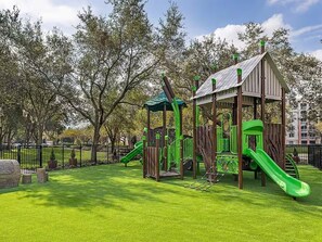 A playground with a slide and climbing structures, surrounded by a fenced area and trees. - King Villa Resort with Balcony near Orlando’s I-Drive (Orlando)